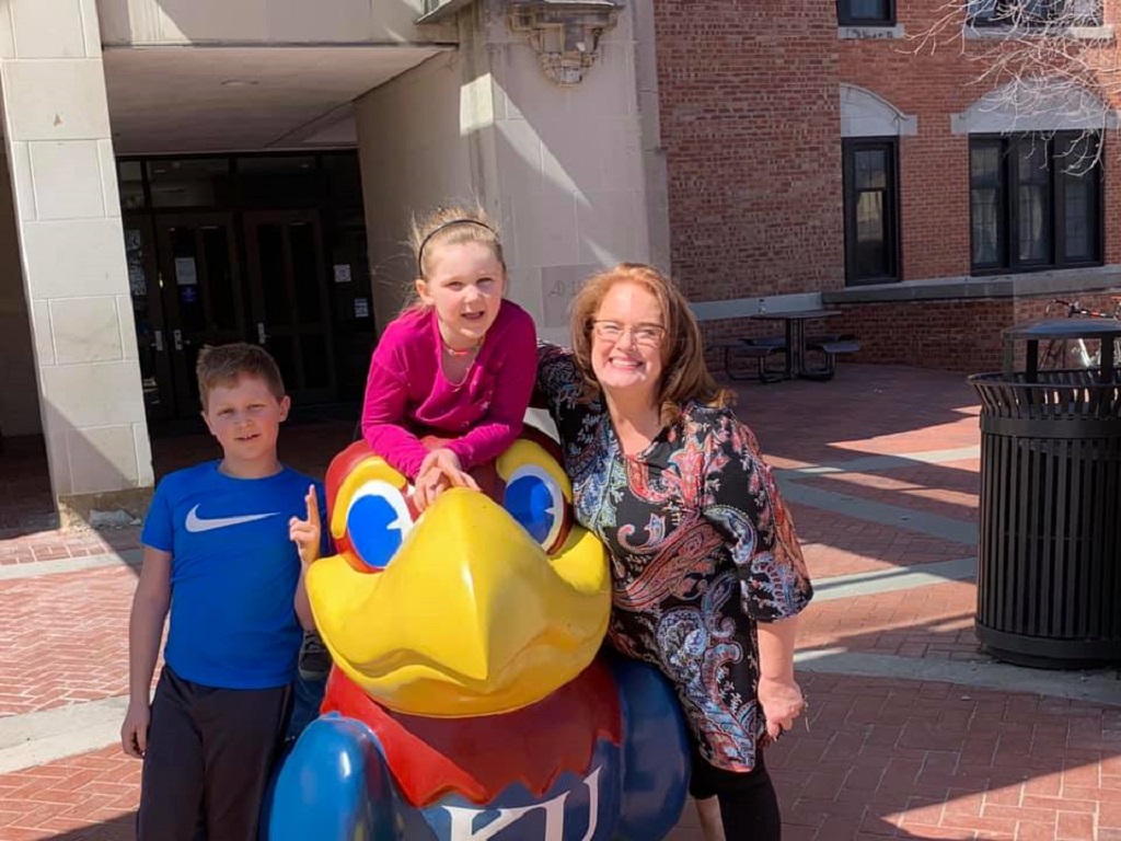 Maggie Mnayer a current Ph.D. student standing next to a large jayhawk with two children