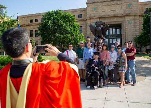 man in graduation gown is taking a photo of people posing in front of Strong Hall